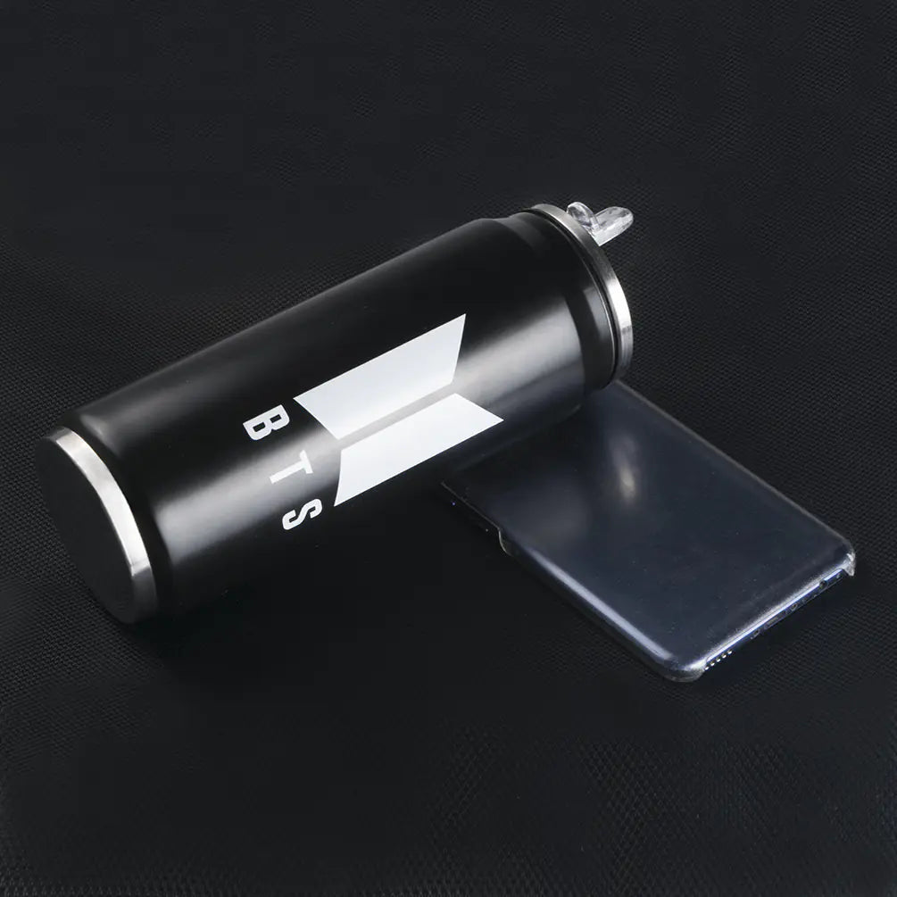 BTS Bulletproof Coffee Cup placed beside a smartphone on a dark background.